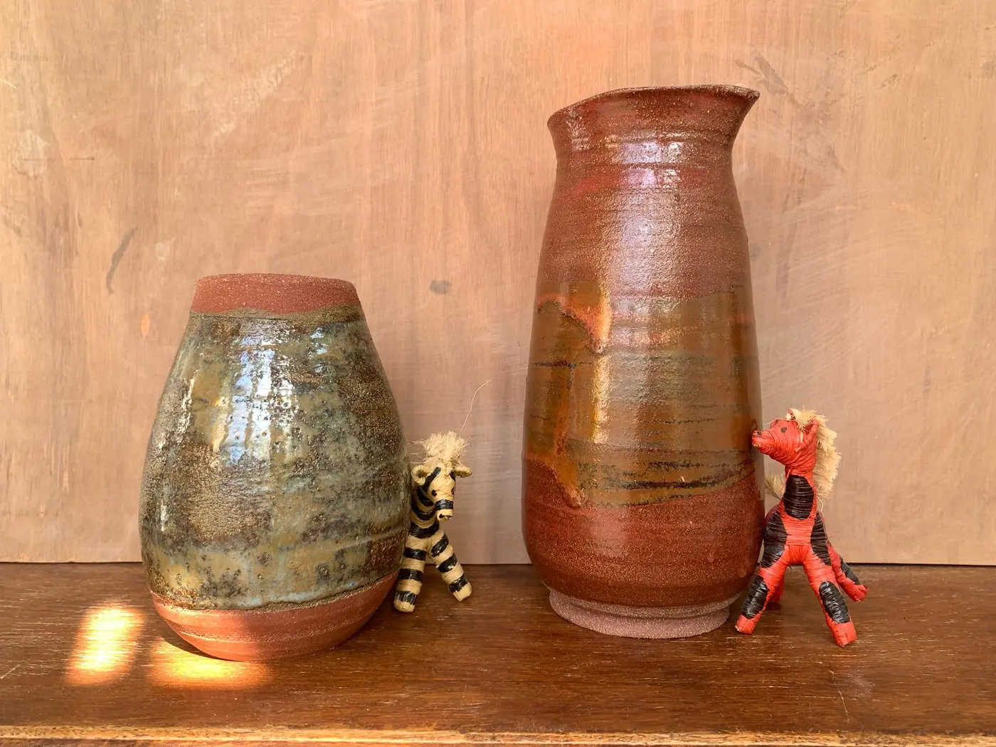 Deux vases aux tons ocre et terre cuite posés sur une étagère en bois